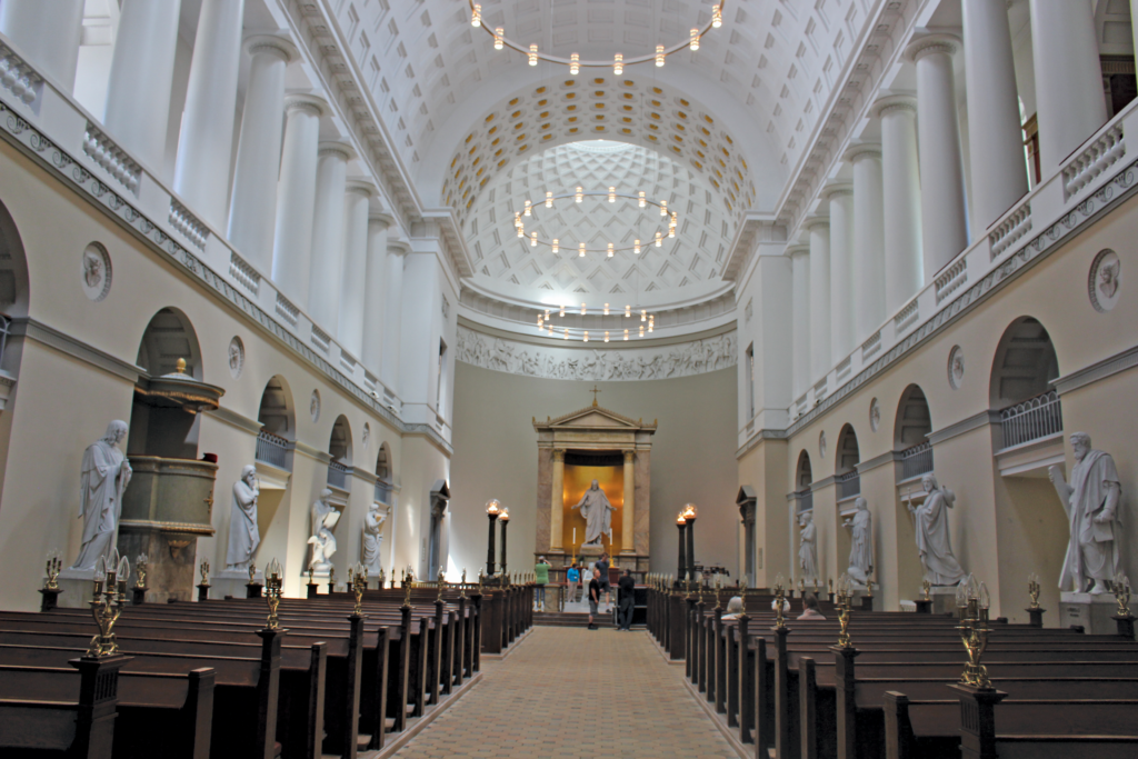The center aisle of the Church of Our Lady, looking toward the front, with dome above the altar and the Christus
